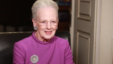 Königin Margrethe von Dänemark kündigt im TV an Silvester ihre Abdankung an. Dabei trägt sie einen lila Pullover mit einer silbernen Brosche, glänzende Ohrstecker und ihr weißes Haar ist edel zurückgesteckt.