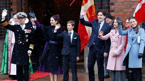 Dänische Königsfamilie: König Frederik, Königin Mary und ihre Kinder Prinz Vincent, Kronprinz Christian und die Prinzessinnen Josephine und Isabella stehen vor der Kathedrale schön aufgereiht und winkend. Die Prinzessinnen tragen wärmende Mäntel und die Königin eine Stola. Die Prinzen haben schicke dunkle Anzüge an und der König trägt seine Uniform.