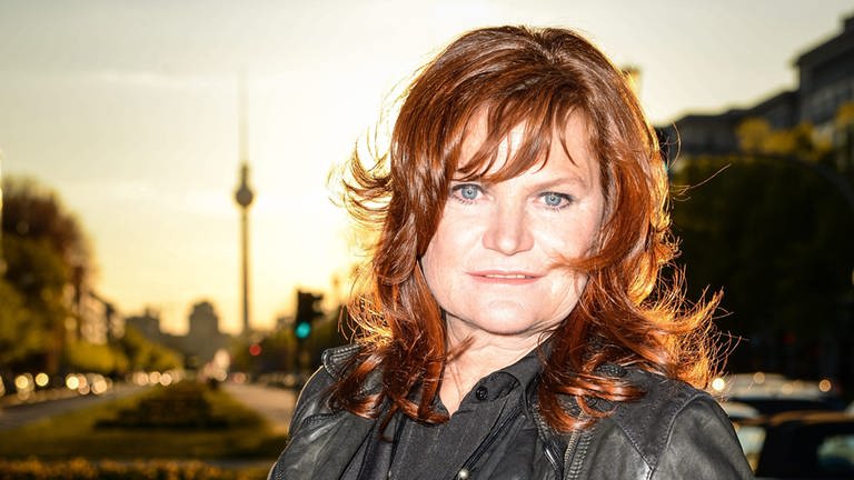 Die Sängerin und Kabarettistin Pe Werner steht mit einer schwarzen Lederjacke im Sonnenuntergang, im Hintergrund ist der Berliner Fernsehturm zu sehen.
