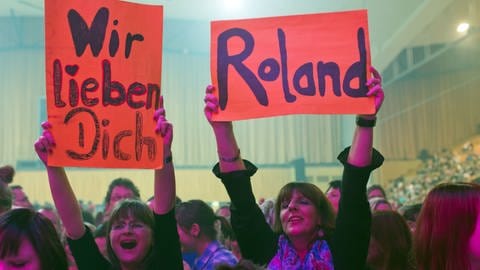Zwei weibliche Fans von Schlagerstar Roland Kaiser mit Schildern, auf denen "Wir lieben Dich, Roland" steht