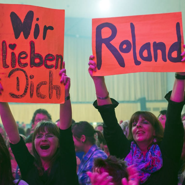 Zwei weibliche Fans von Schlagerstar Roland Kaiser mit Schildern, auf denen "Wir lieben Dich, Roland" steht (Foto: dpa Bildfunk, Picture Alliance)