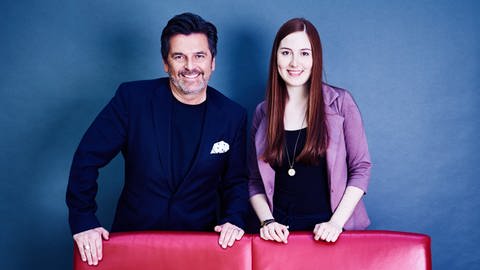 Schlagersänger Thomas Anders steht mit Musikredakteurin Andrea Mayer hinter einem roten Sofa. Beide tragen schicke Blazer und lächeln nach dem Interview in die Kamera. (Foto: SWR)