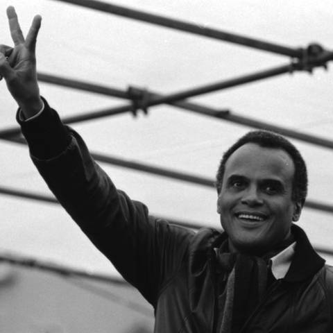 Schwarz-weiß Foto des Sängers, Schauspielers und Menschrechtsaktivists Harry Belafonte, der mit seinen Fingern ein Peace-Zeichen in die Luft hält. (Foto: picture-alliance / Reportdienste, picture alliance / Klaus Rose)