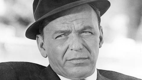 Der amerikanische Sänger und Schauspieler Frank Sinatra mit einem Becher in der Hand und einem Anzug und Hut bekleidet schaut in die Ferne. (Foto: dpa Bildfunk, Picture Alliance)