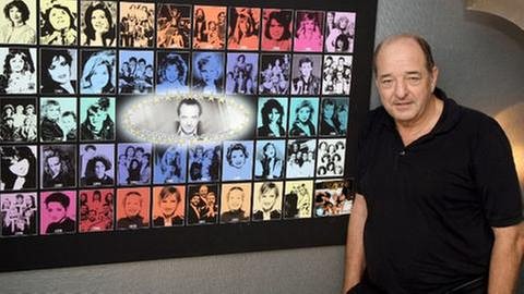 ESC Legende Ralph Siegel vor einem Bild aller Künstler, die mit seinen Kompositionen am Grand Prix teilgenommen haben. (Foto: IMAGO, Imago -)