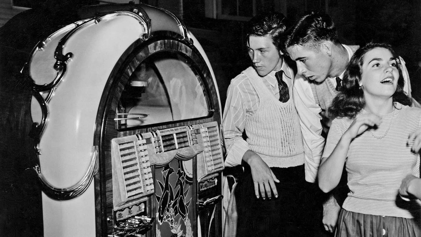 Schwarz-weiß Bild aus den 1950er-Jahren. Junge Menschen stehen vor einer Jukebox. (Foto: picture-alliance / Reportdienste, picture alliance / World History Archive | -)