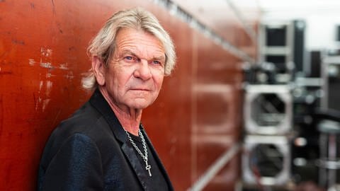 Portrait von Schlagersänger Matthias Reim in einer schwarzen Jacke vor einer roten Mauer. (Foto: dpa Bildfunk, Picture Alliance)