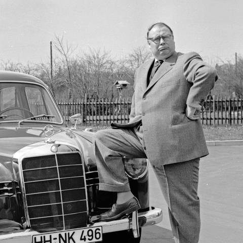 Der deutsche Schauspieler und Sänger Heinz Erhardt posiert stolz an seinem Mercedes Benz. Bild in schwarz-weiß.