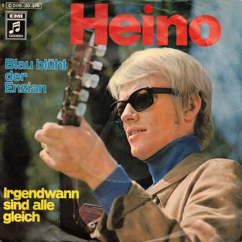 Sänger Heino mit Sonnenbrille in jungen Jahren mit Gitarre in der Hand. Er trägt einen blauen Rollkragenpullover und eine beige Jacke drüber. Das Foto dient als Cover für die Lieder "Blau blüh der Enzian" und "Irgendwann sind alle gleich" (Foto: SWR, Coverscan: Columbia)