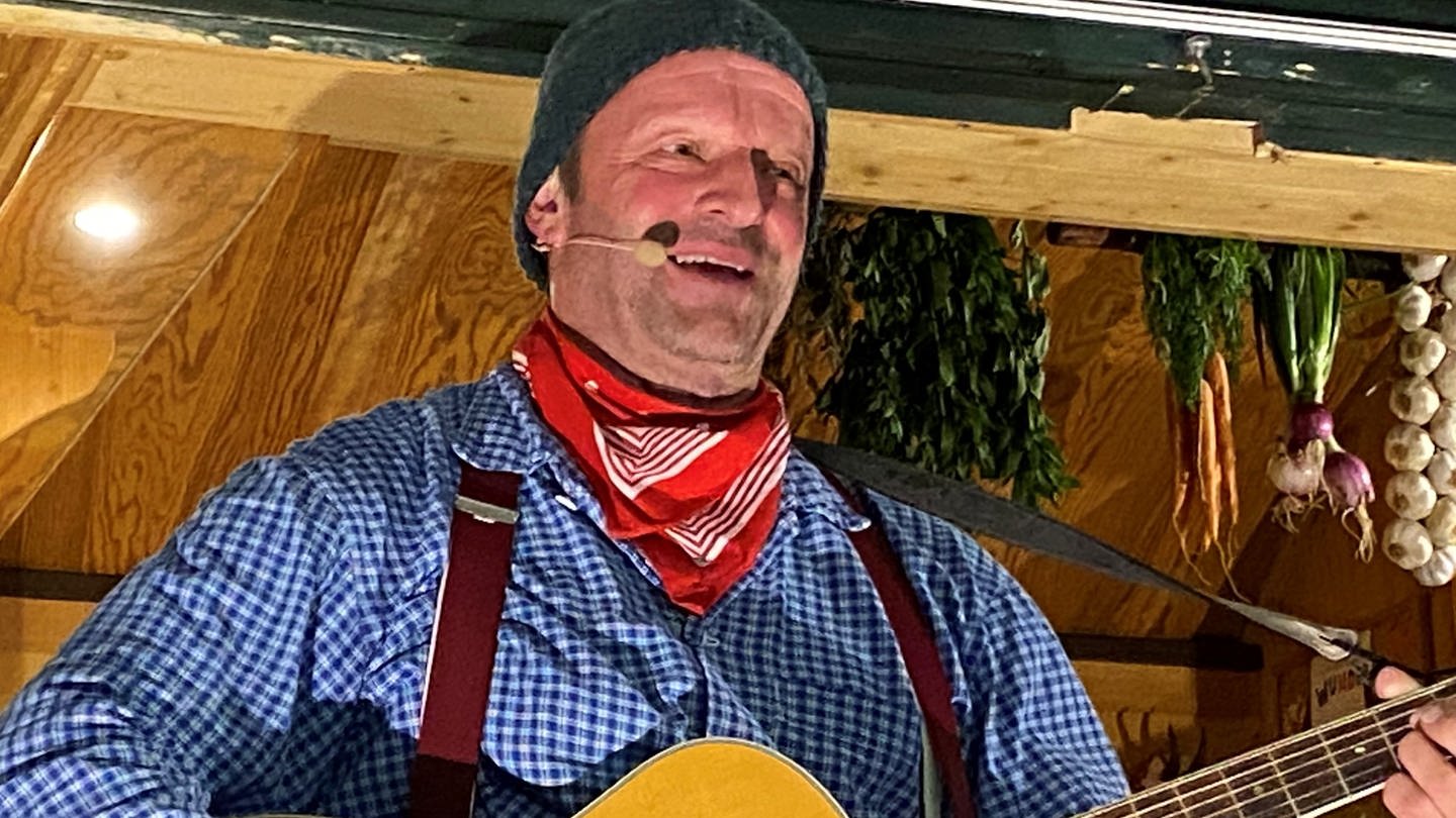 Der Komiker Fidelius Waldvogel aus dem Schwarzwald steht mit der Gitarre auf einer Bühne und singt in ein Mikrofon rein. (Foto: SWR, Matthias Zeller)
