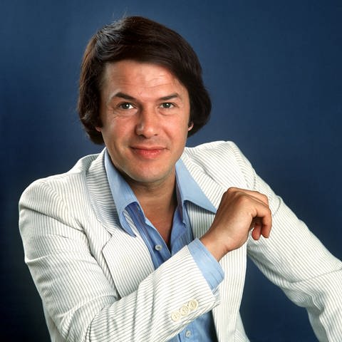 Salvatore Adamo posiert in einem weißen Anzug für ein Porträtbild.