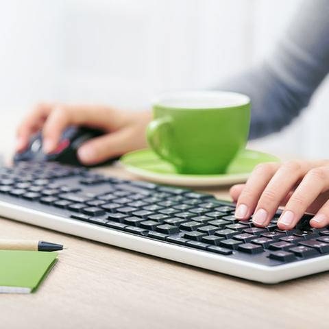 Eine Frau sitzt vor ihrem Computer und einer grünen Tasse und tippt in ihre Tastatur (Foto: Colourbox)