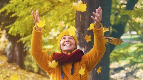 Eine Frau wirft Herbstlaub in die Luft