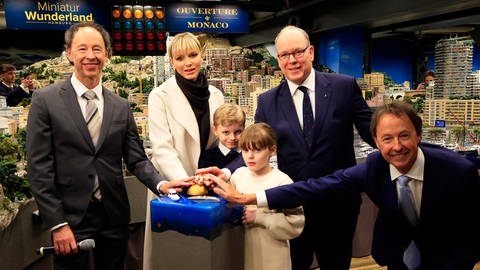 Fürst Albert II. von Monaco und seine Familie stehen mit den Gründern des Miniatur Wunderlandes, Gerrit Braun und Frederik Braun, vor der Kulisse von Mini-Monaco in Hamburg und eröffnen mit einem goldenen Button den neuen Modellabschnitt.