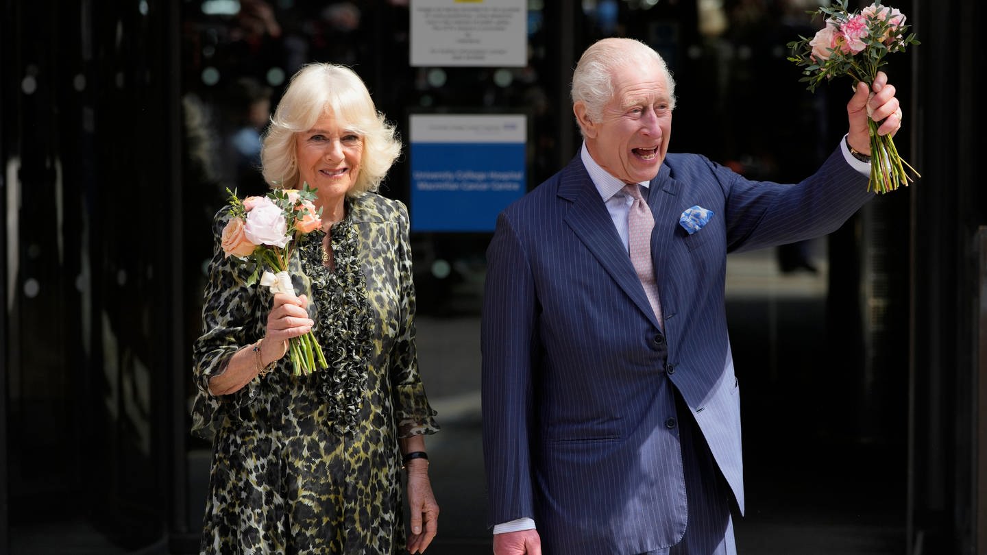 König Charles III. und seine Frau Königin Camilla besuchen gut gelaunt eine Krebszentrum. Beide tragen kleine Sträuße in der Hand. (Foto: picture-alliance / Reportdienste, picture alliance/dpa/AP | Kin Cheung)