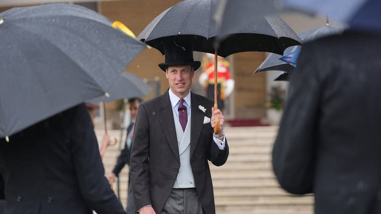 Prinz William mit Anzug, Zylinder und Regenschirm auf der Gartenparty vor dem Buckingham Palast 