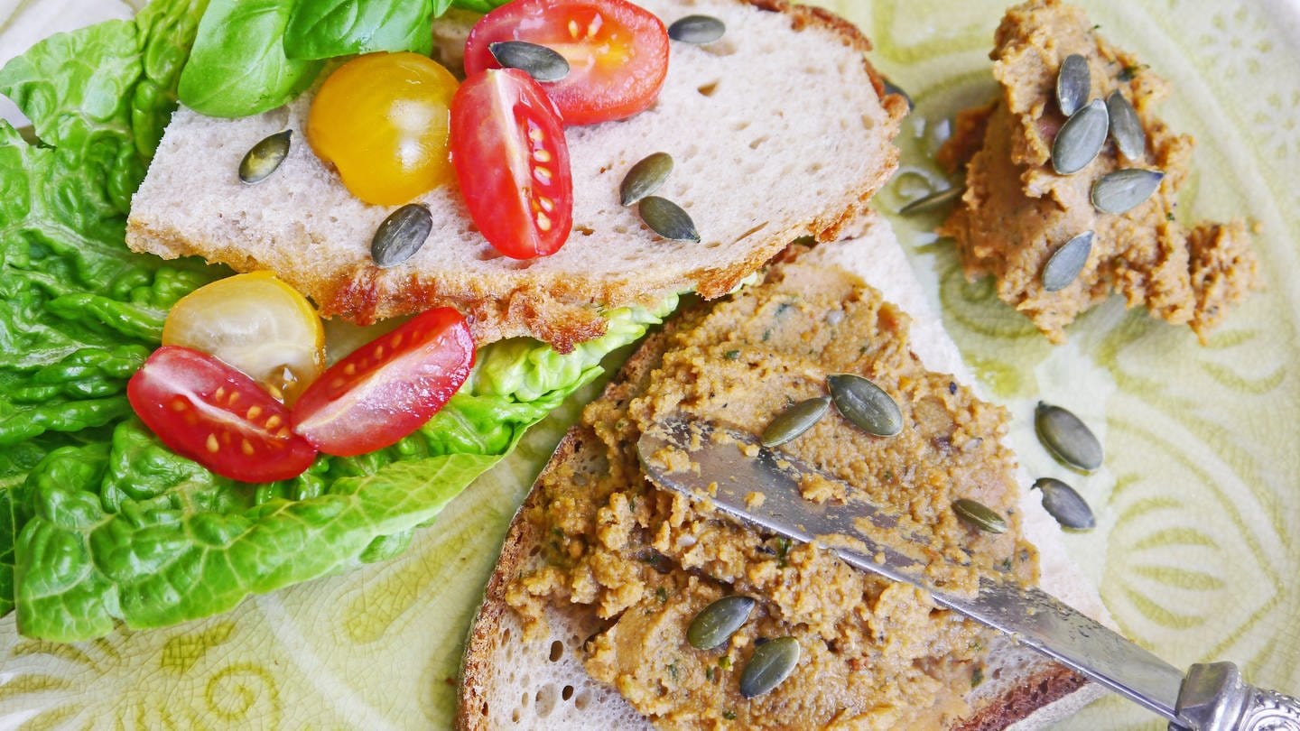 zwei halbe Brotscheiben mit einem Salatblatt und kleinen Tomaten und einem rötlichen Brotaufstrich mit einem verzieren Messer (Foto: SWR, Stefanie Kühn)