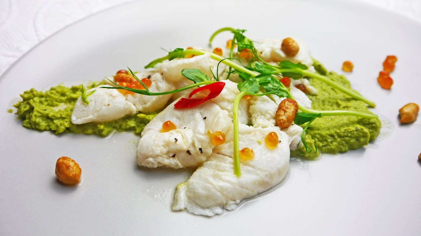 weißer Teller mit grünem Erbsenpüree, darauf helle Fischstücke mit Chili, Nüssen und hellrosa Lachskaviar dekoriert (Foto: SWR, Stefanie Kühn)