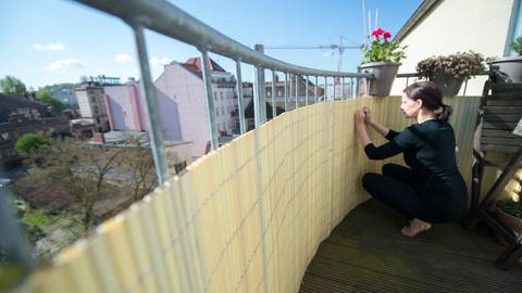 Eine Frau befestigt an ihrem Balkon einen Sichtschutz