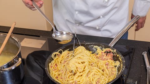 Rezept: Für original Spaghetti Carbonara Nudelwasser statt Sahne verwenden. Mit einer Schöpfkelle zu den Nudeln in die Pfanne geben. (Foto: SWR, Corinna Holzer)