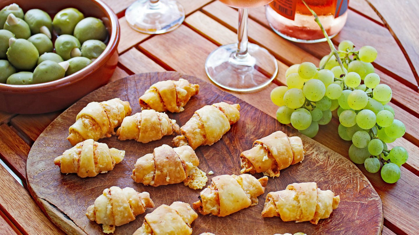 Holzbrett mit Käsehörnchen, daneben Trauben und ein Glas Rose-Wein (Foto: SWR, Imogen Voth)