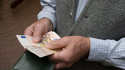 Ein älterer Mann mit Strickweste hält mehrere 50-Euro-Scheine aufgefächert in der Hand (Foto: picture-alliance / Reportdienste, Picture Alliance)