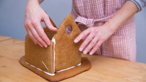 Eine Frau klebt ein Lebkuchenhaus mit Zuckerguss zusammen (Foto: picture-alliance / Reportdienste, Florian Schuh / dpa Themendienst)