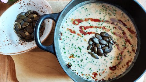gußeiserner Topf mit heller Suppe mit Kürbiskernen, daneben eine kleine Schüssel mit Kürbiskernen (Foto: SWR, Jens Alinia)