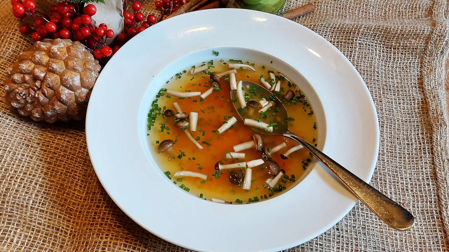 weißer Teller mit klarer Suppe mit Pilzen als Enlage. Daneben Weihnachtsschmuck. (Foto: SWR, Jens Alinia)
