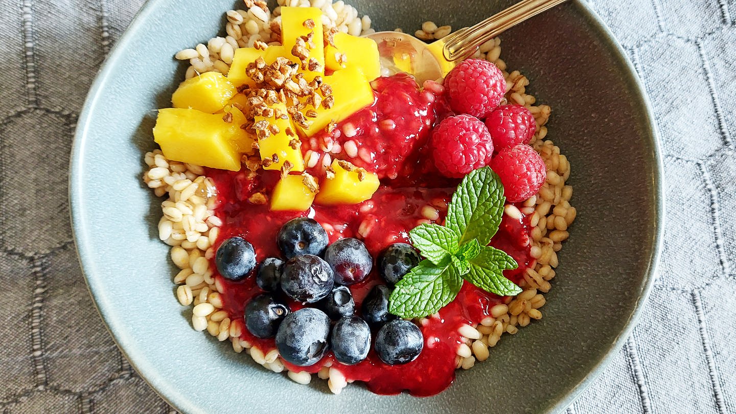 Porridge aus Graupen mit Blaubeeren und Himbeeren und Mango in einer Schüssel. Minzblätter als Deko. (Foto: SWR, Jens Alinia)