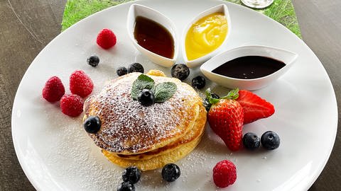 Stapel Pancakes auf einem weißen Teller mit Beeren drumherum, daneben Schälchen mit verschiedenen Saucen, neben dem Teller ein Glas Eierlikör (Foto: SWR, Vanessa Siemers)