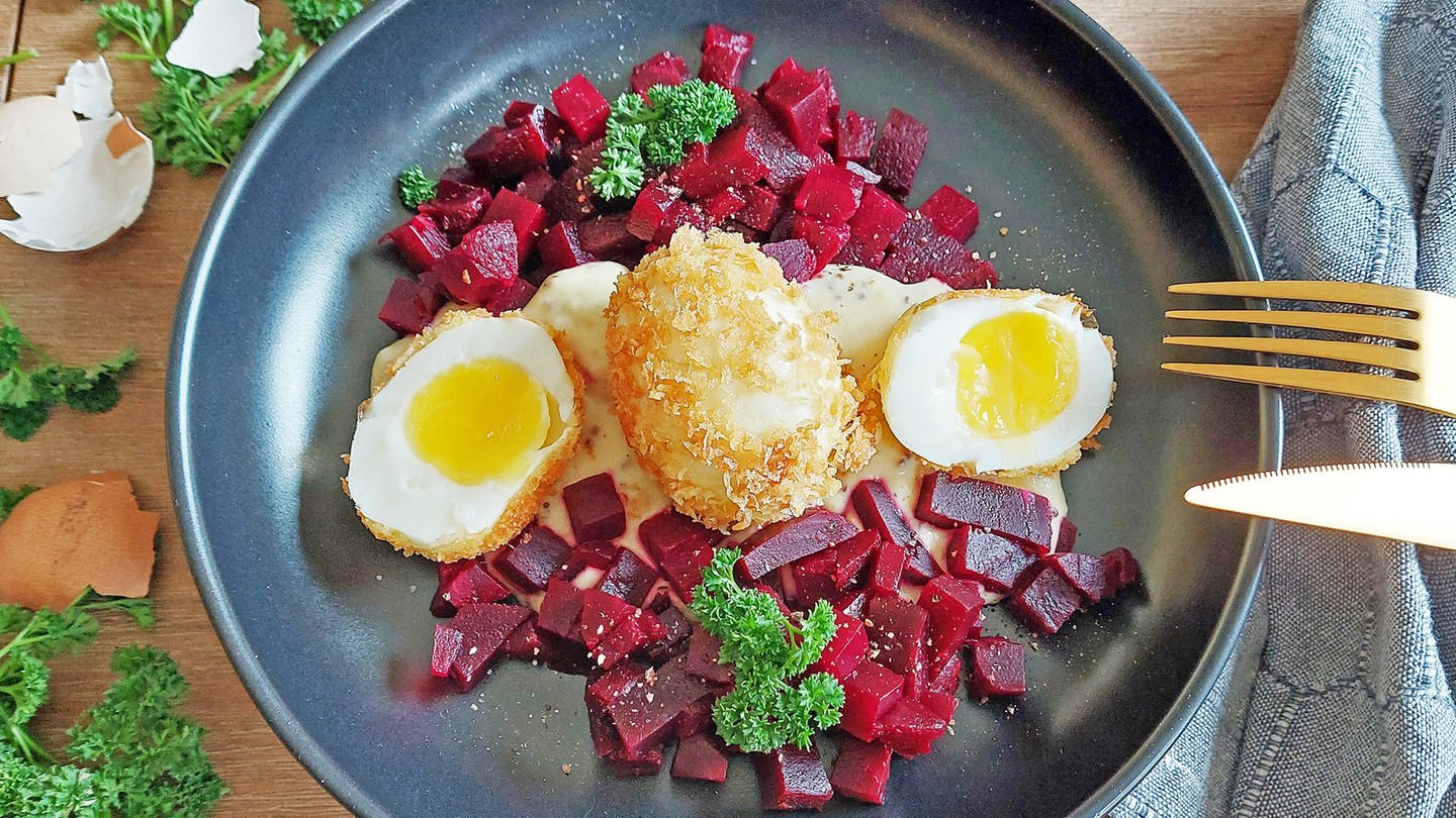 frittierte Eier, zwei Hälften und eins ganz auf auf einem Salatbett mit roter Bete, daneben goldenes Besteck und Eierschalen (Foto: SWR, Jens Alinia)