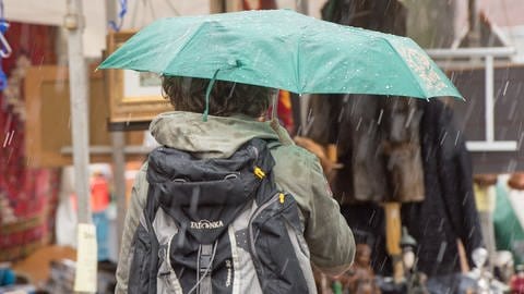 Ein Besucher auf einem Flohmarkt schützt sich mit einem Regenschirm vor Hagel und Regen.  (Foto: dpa Bildfunk, picture alliance / dpa | Maurizio Gambarini)