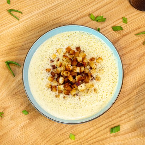 Die Lauchcremesuppe ist in einem Teller mit Croutons und Speck angerichtet. Der Teller steht auf einem Holztisch. (Foto: SWR, Corinna Holzer)