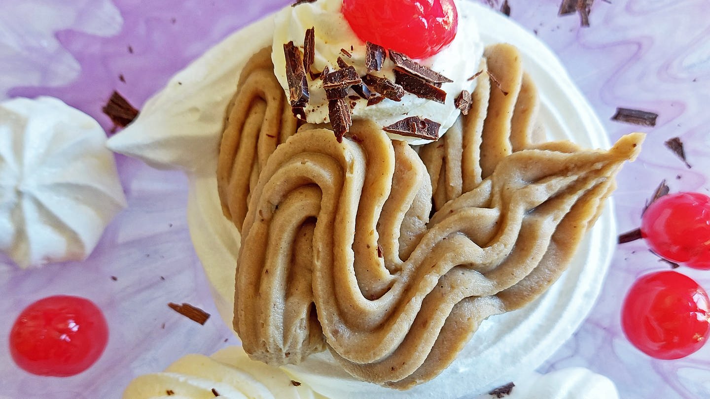 Süße Maronencreme mit Baiser: Das Dessert von oben aus der Totale fotografiert. Es ist mit roten Cocktailkirschen garniert. Auf dem Teller daneben liegen mehrere Stücke von Baiser. (Foto: SWR, Jens Alinia und Corinne Schied)