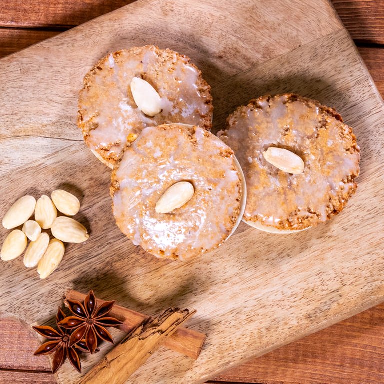 Nach dem Backen liegen die Lebkuchen auf einem Holzbrett. Die Elisenlebkuchen sind wie im Rezept beschrieben mit Zuckerguss glasiert und Mandeln dekoriert.  (Foto: SWR, Corinna Holzer)