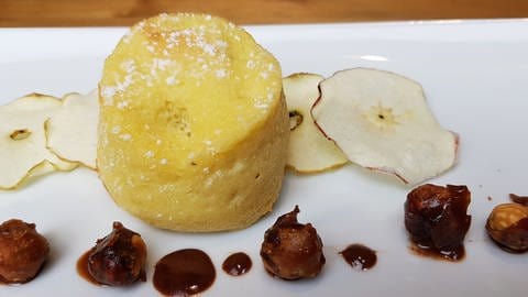 Rezept: Weißer Teller mit einem Apfel-Clafoutis auf getrockneten Apfelscheiben mit Nüssen als Deko (Foto: SWR, Stefanie Kühn)