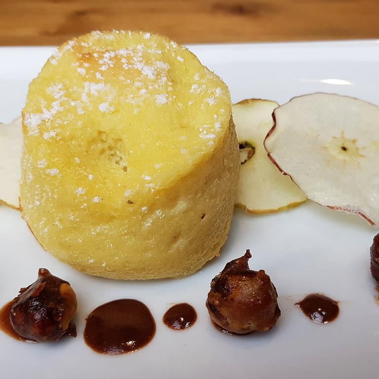 Rezept: Weißer Teller mit einem Apfel-Clafoutis auf getrockneten Apfelscheiben mit Nüssen als Deko (Foto: SWR, Stefanie Kühn)