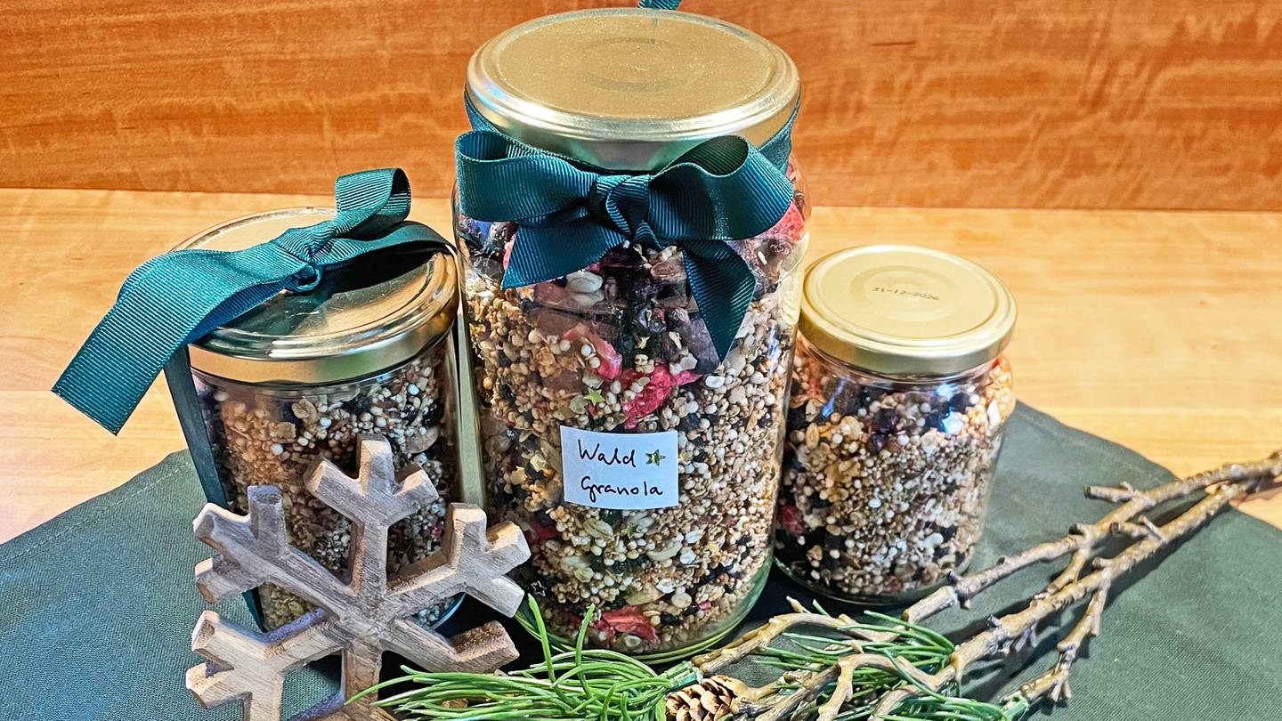 Rezept für Knuspermüsli (Granola): Drei Gläser mit Müsli gefüllt, mit Schleifen dekoriert auf einem Tisch, grüne Zweige und ein Holzstern als Deko daneben. (Foto: SWR, Alexandra Daub)