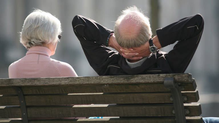 Rente und Altersvorsorge - entspannt in den Ruhestand: Ein Rentnerpaar sitzt auf einer Parkbank und ist von hinten zu sehen. Der Mann lehnt sich entspannt zurück und verschränkt die Hände hinter dem Kopf. (Foto: dpa Bildfunk, Picture Alliance)