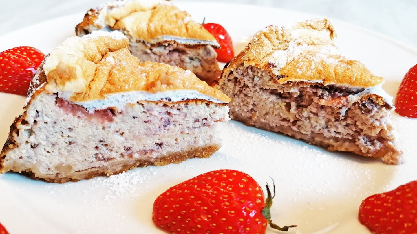 hellbrauner Kuchen mit Erdbeeren an der Seite und einem Teller mit Erdbeeren mit Sahne daneben (Foto: SWR, Stefanie Kühn)