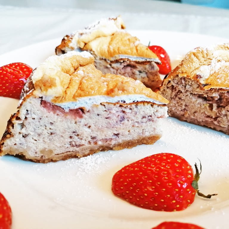 hellbrauner Kuchen mit Erdbeeren an der Seite und einem Teller mit Erdbeeren mit Sahne daneben (Foto: SWR, Stefanie Kühn)