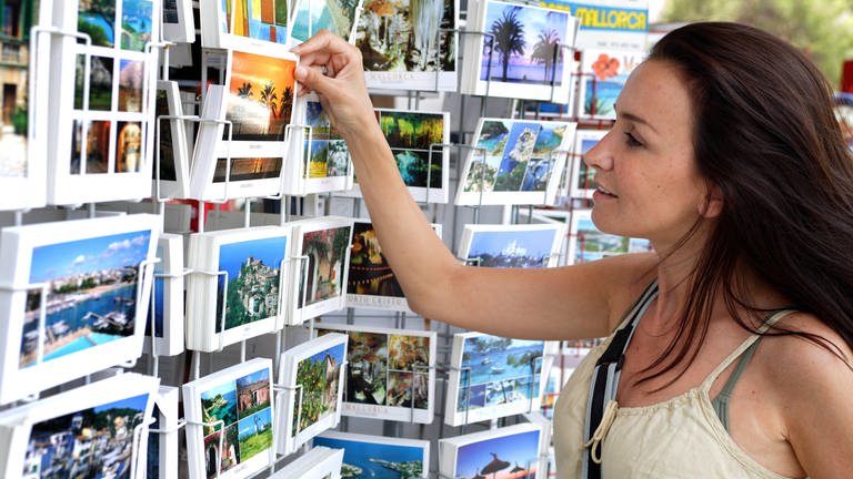 Eine Frau sucht sichim Kiosk eine Postkarte aus