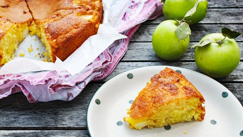 Stück Rührteigkuchen mit Äpfeln auf Teller, daneben ein angeschnittener Kuchen in Backform und Äpfel (Foto: SWR, Imogen Voth)