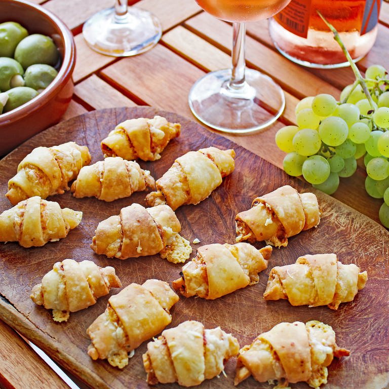 Holzbrett mit Käsehörnchen, daneben Trauben und ein Glas Rose-Wein (Foto: SWR, Imogen Voth)