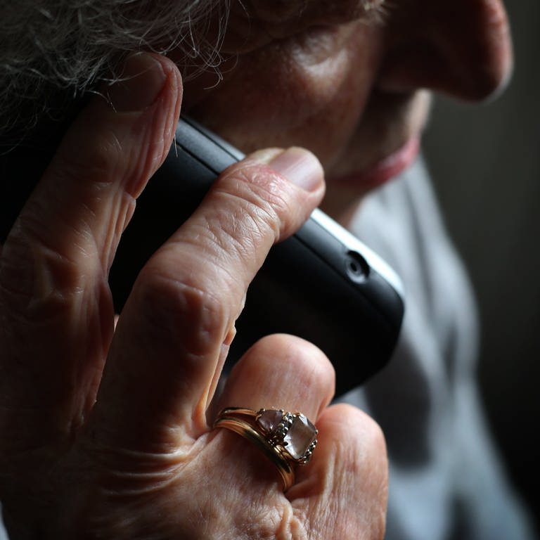 Eine ältere Frau hält vor dunklem Hintergrund den Telefonhörer ans Ohr