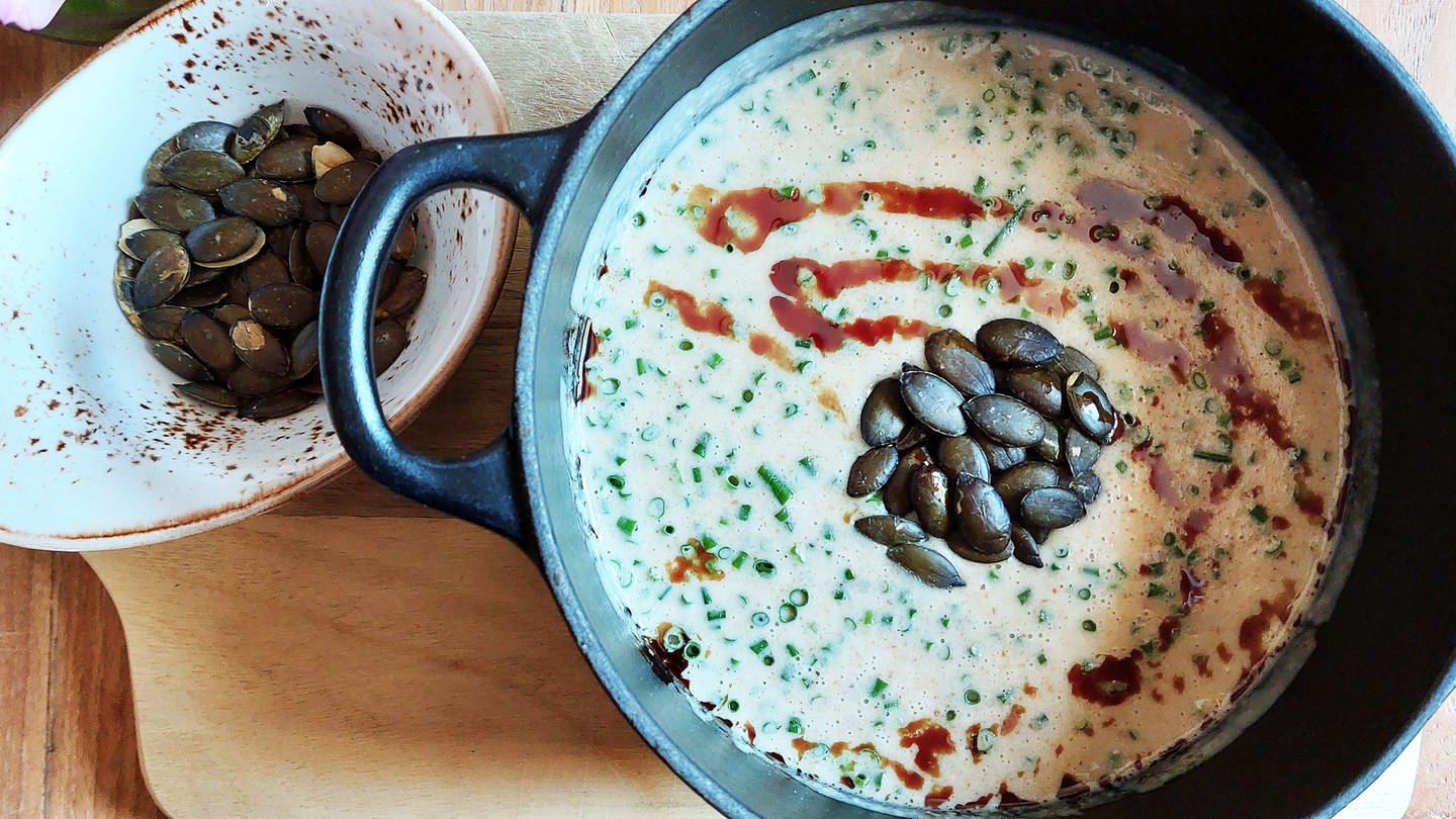 gußeiserner Topf mit heller Suppe mit Kürbiskernen, daneben eine kleine Schüssel mit Kürbiskernen (Foto: SWR, Jens Alinia)