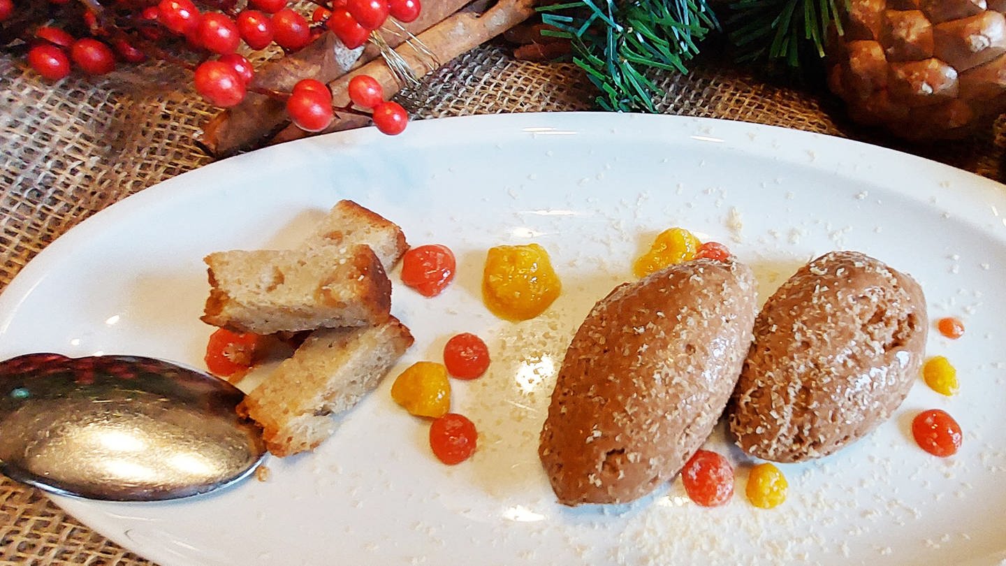 weißer Teller mit Nocken von brauner Mousse mit kandierten Früchten. Daneben Weihnachtsdeko. (Foto: SWR, Jens Alinia)