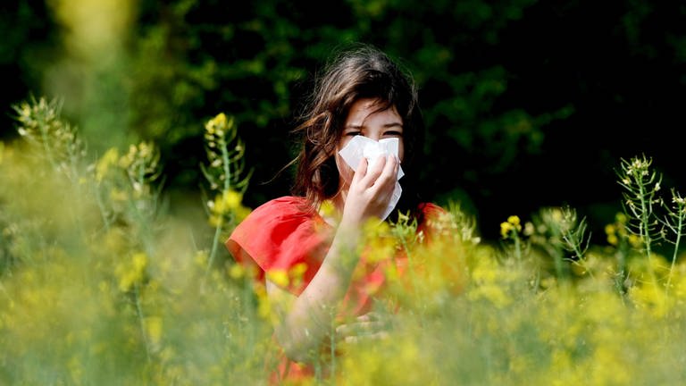 Eine Frau putzt sich zwischen Blüten die Nase.
