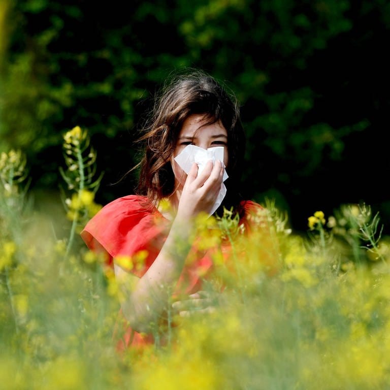 Eine Frau putzt sich zwischen Blüten die Nase.